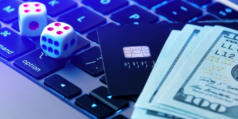 パソコンの上にサイコロやクレジットカード、ドルが置かれている様子